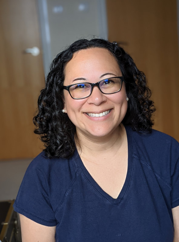 Photo of smiling woman with black curly hair and black glasses in a V-neck navy blue T-shirt